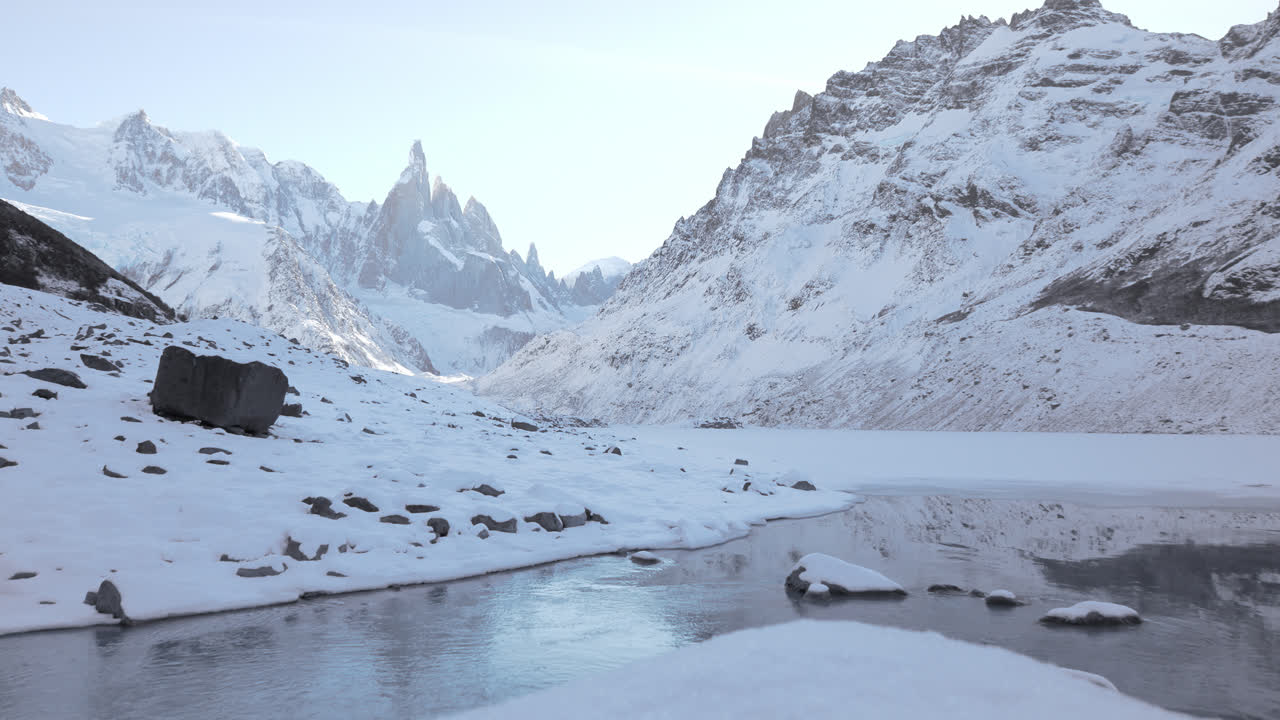 Static shot of Cerro Torre massif rising above Laguna Torre, featuring flowing icy water, snow covered slopes, and dramatic Patagonian peaks