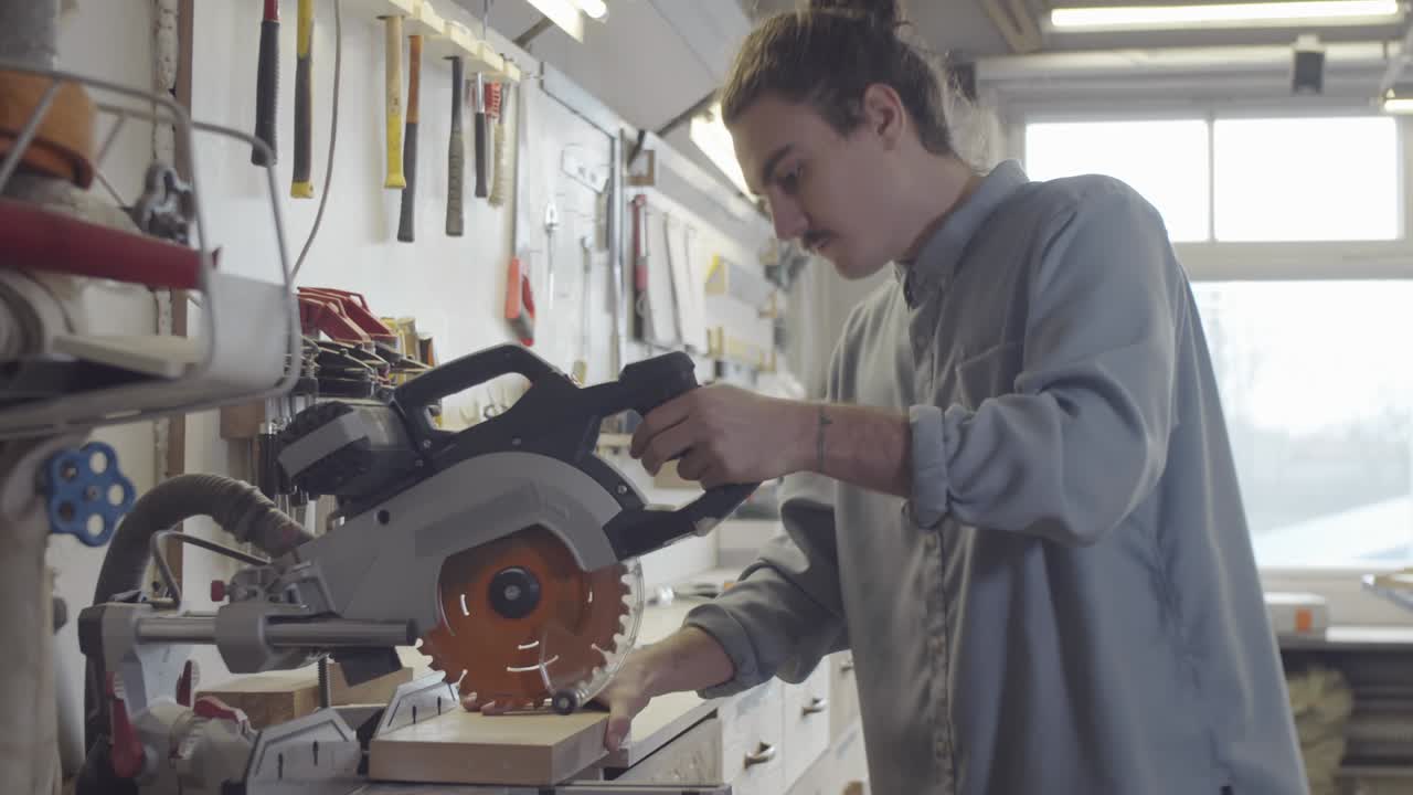 joven carpintero cortando tabla de madera en pedazos en una sierra de mitra en el taller