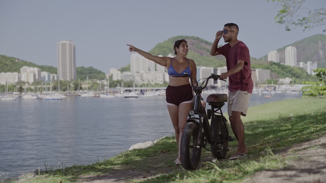 Couple Walking with Bicycle Along Waterfront with City and Mountain Views