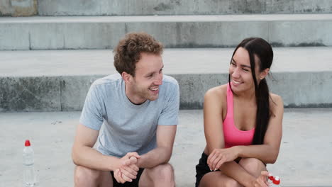 Happy-Sportive-Couple-Sitting-On-Stairs-And-Talking-To-Each-Other-After-Running-Session-In-The-City