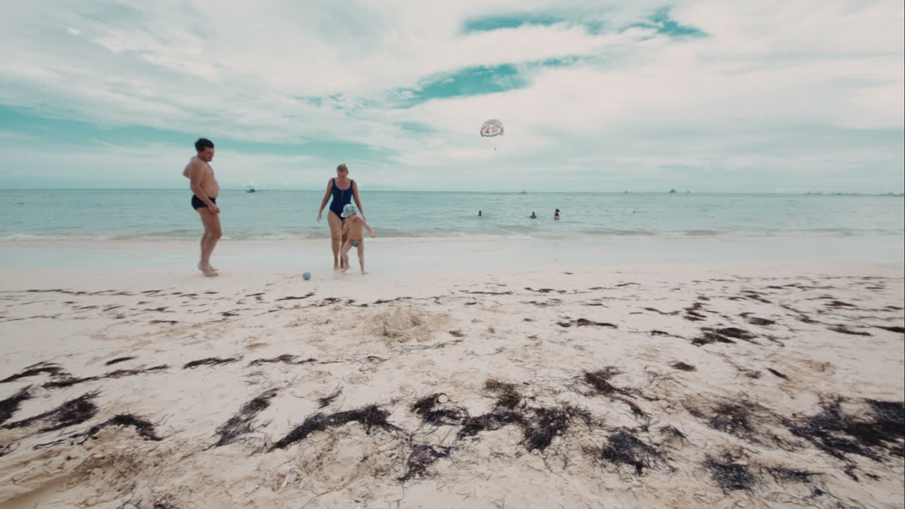 una feliz familia de tres personas jugando a la pelota en la playa