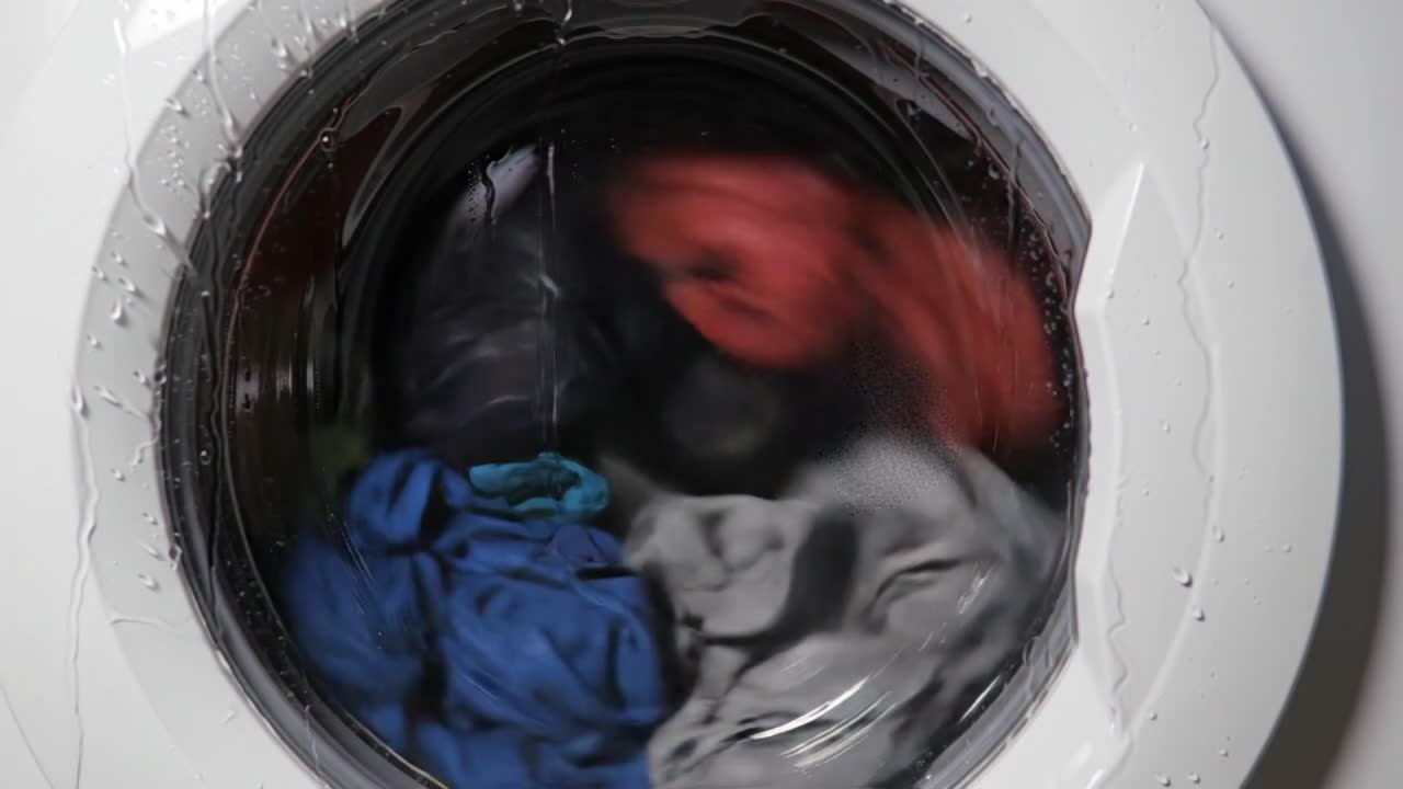 Clothes tumble in a front-loading washing machine filled with water, showcasing a variety of colors and fabrics as the cycle progresses.