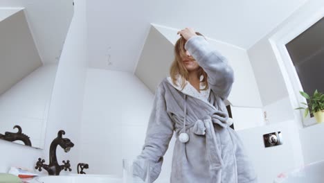 a young woman in a bathrobe in the home bathroom looks in the mirror