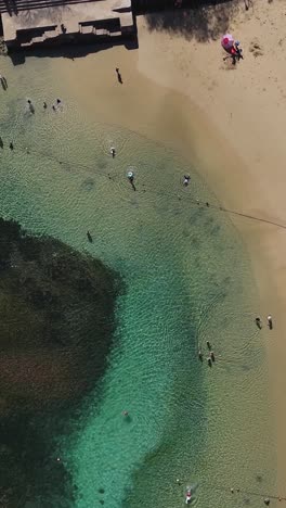 People-on-a-crystalline-beach-in-Huatulco,-vertical-mode