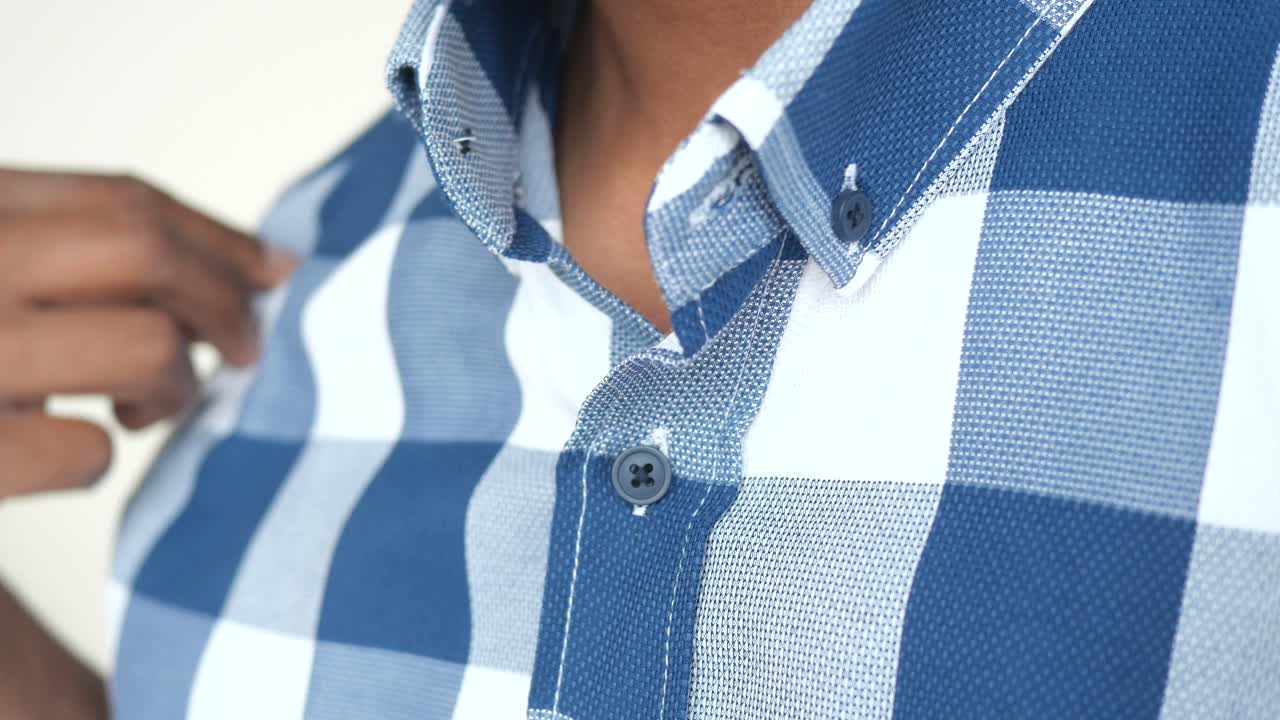 un hombre abotonando una camisa a cuadros azul