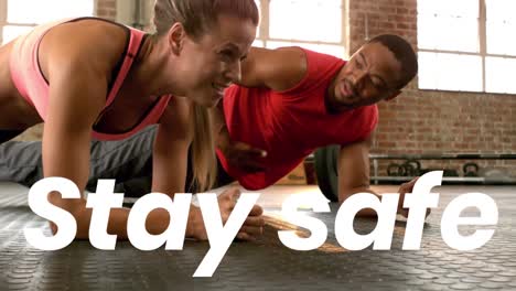 animation of stay safe text over woman and man doing plank in gym