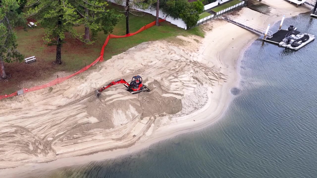 Piccolo escavatore che sposta sabbia in un cantiere edile fronte mare