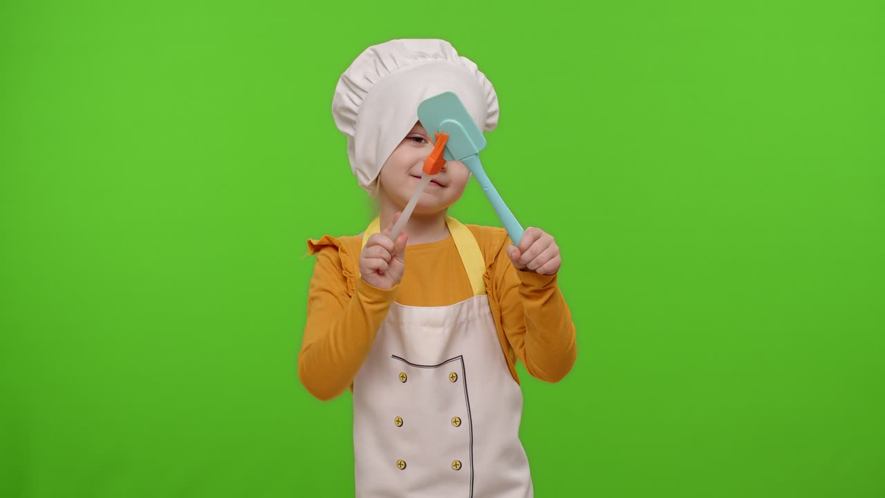 niña vestida con un delantal como chef cocinero bailando espátula en fondo de clave cromada, cámara lenta