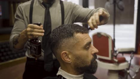 barbero rociando agua en el cabello del cliente y peinándolo - de cerca