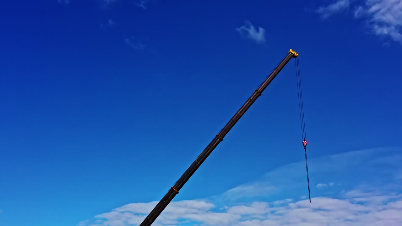 Chains hanging from Tall Crane Arm Reaching High Into Clear Blue Sky With Clouds on Bright Sunny Day