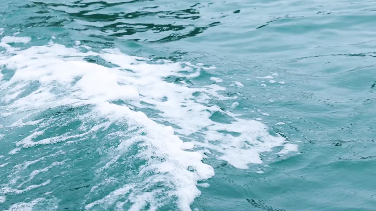 Close-up view of turquoise waters with dynamic ripples and foamy waves creating a mesmerizing pattern.