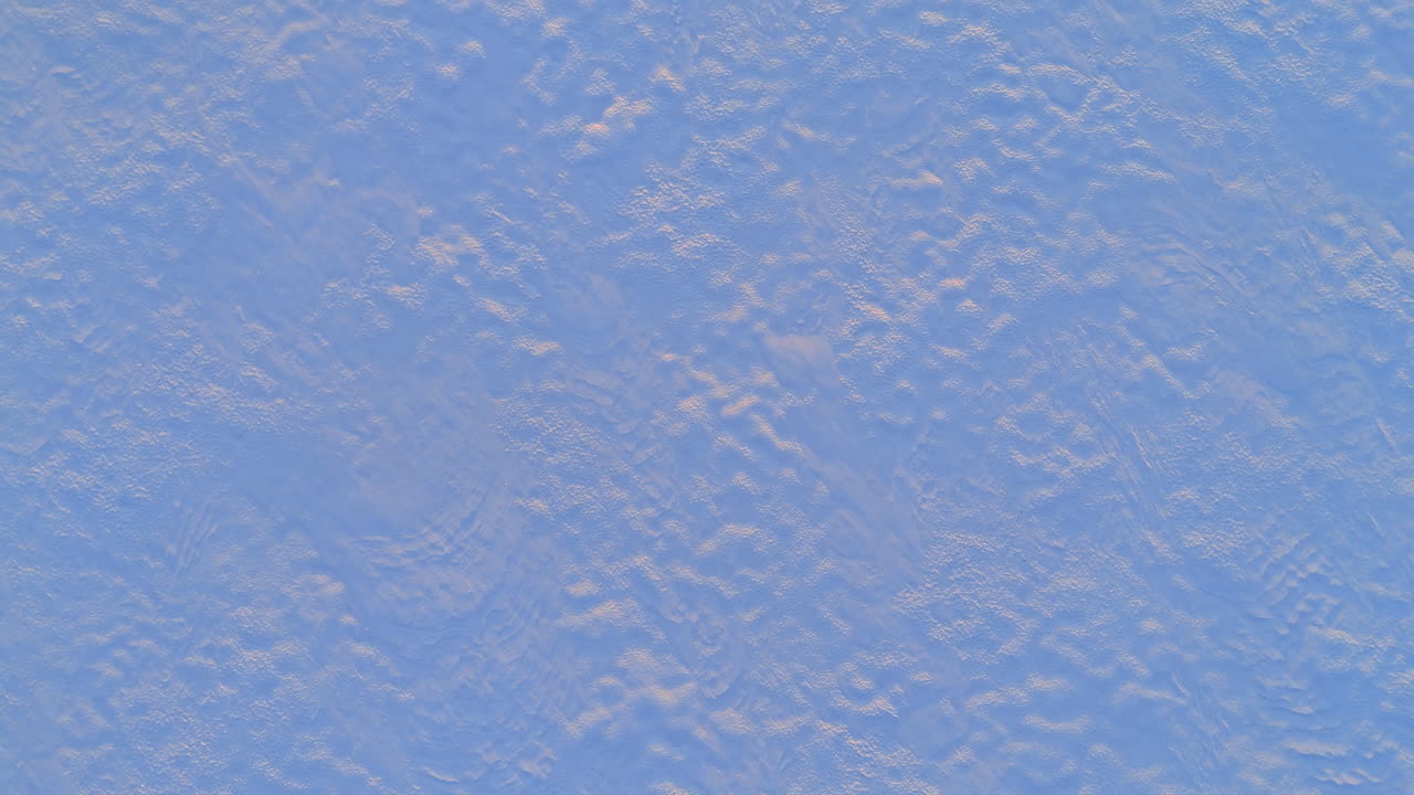 Texture of wind blown snow surface during sunset light. Close up aerial view of snow patterns and ice crystals illuminated by low golden sun