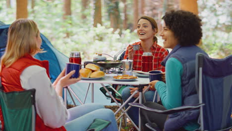 grupo de amigas en vacaciones de campamento en el bosque cocinando comida sentados en una tienda de campaña juntos