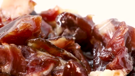 extreme close up of fatty serrano ham pieces rotating on a white surface