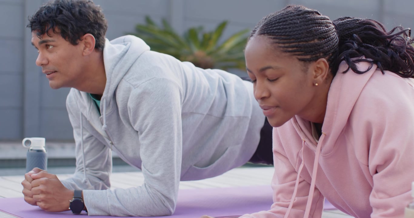 African American couple holding plank on rooftop after resting on purple mats with bottles for core