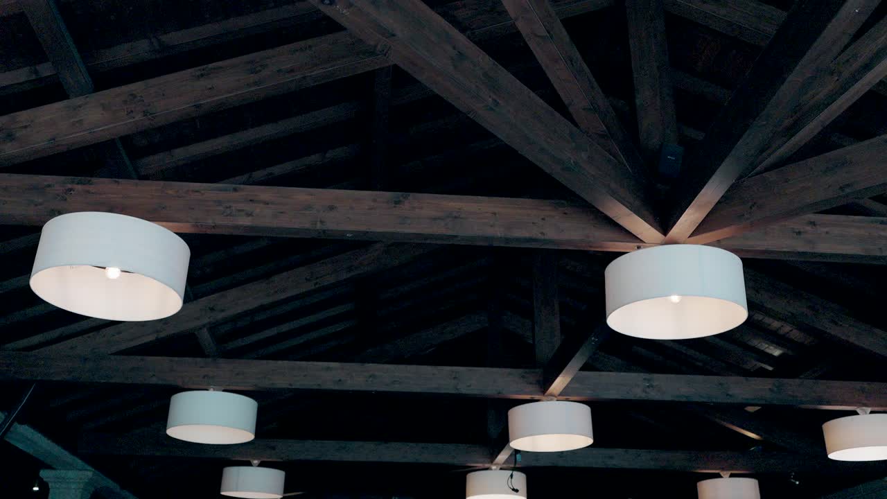 circular ceiling lamps glowing against exposed wooden beams in dim space