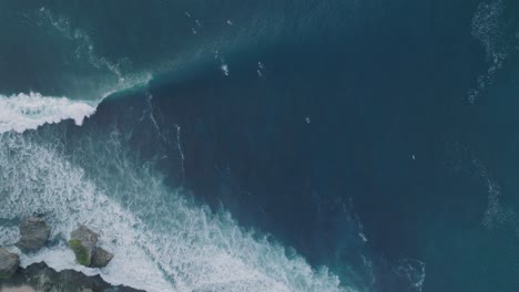 Top-Down-Drone-of-unidentifiable-surfers-at-sunset-with-deep-blue-and-gold-water-at-Padang-Padang,-Bali,-Uluwatu-Indonesia