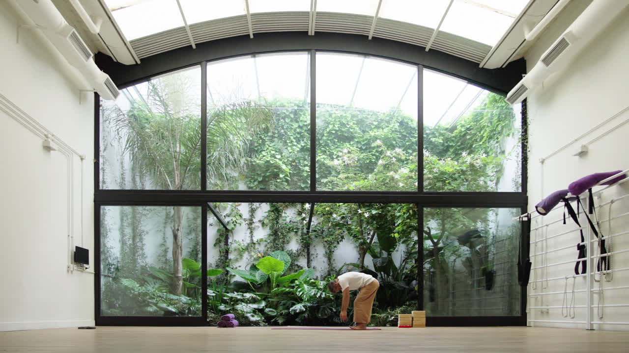Hombre practicando yoga y estiramientos en un estudio luminoso con vista al jardín