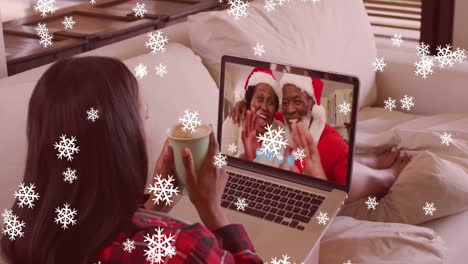 Snowflakes-falling-over-woman-holding-a-coffee-cup-having-a-videocall-on-laptop-during-christmas