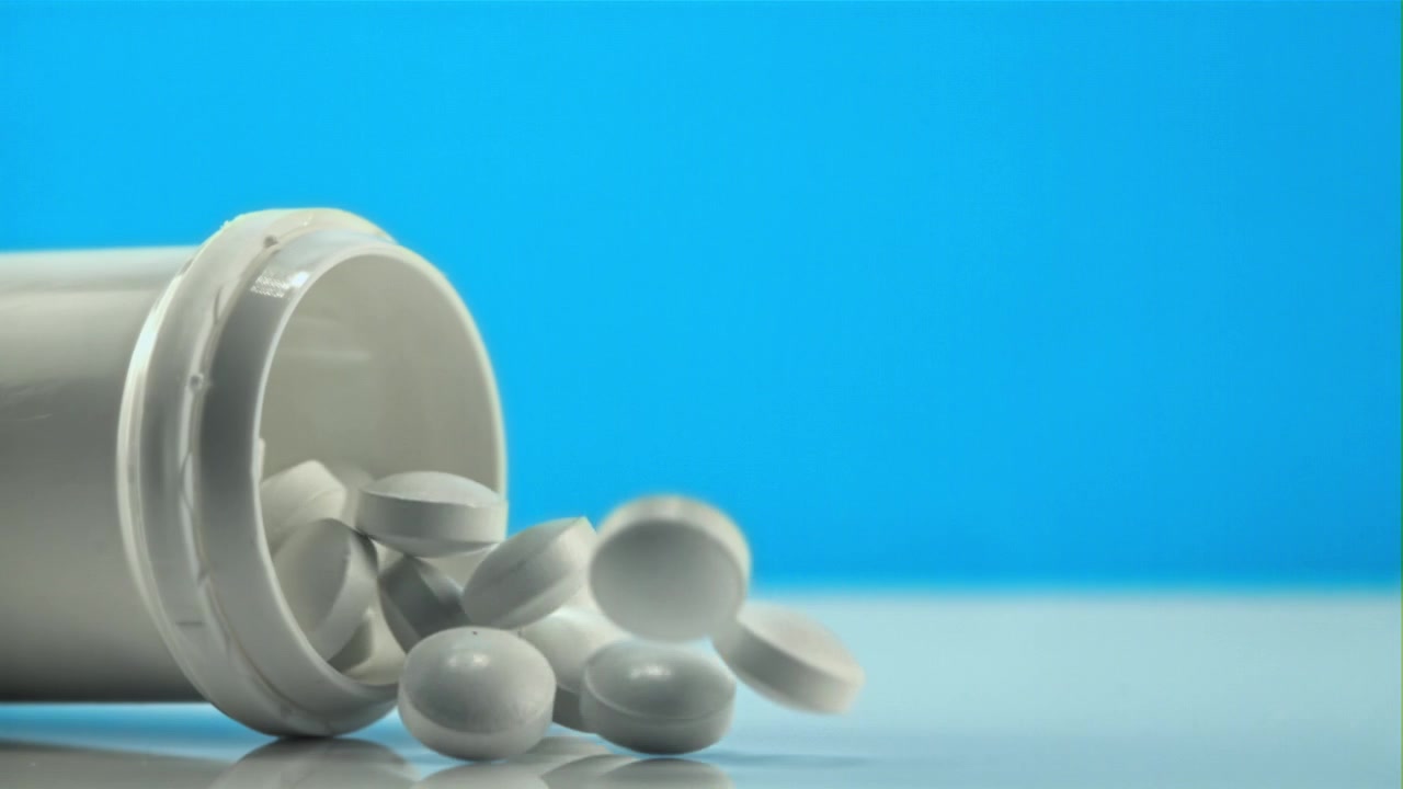 Pillole bianche che cadono da una bottiglia su una superficie riflettente con sfondo blu