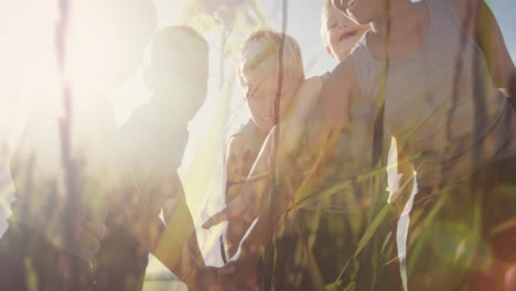animation of sun and grasses over happy diverse schoolchildren stacking hands in outdoor sport class