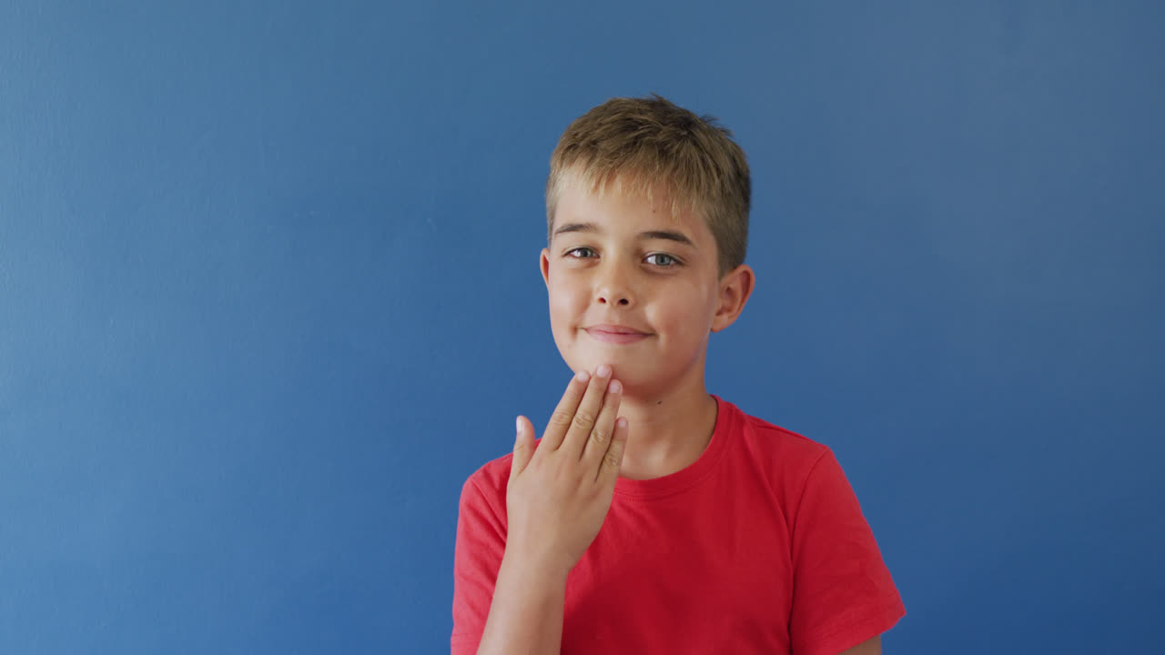 retrato de un niño caucásico feliz usando lenguaje de señas en fondo azul, cámara lenta