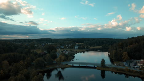 Puente-Sobre-El-Tranquilo-Lago-Con-Coches-Que-Viajan-Cerca-Del-Pueblo-Rodeado-De-Un-Denso-Paisaje-De-Follaje-Durante-El-Atardecer-En-Tleń-En-Polonia