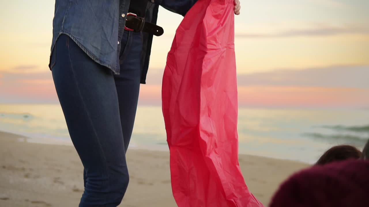 젊은 매력적인 여성은 그녀의 친구들과 함께 해변에 서서 날아가기 전에 불로 랜턴을 들고 있습니다. 친구들