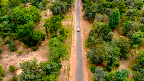 Luftaufnahme,-Die-über-Eine-Alte,-Geflickte,-Zweispurige-Waldstraße-Fliegt,-Wobei-Das-Auto-Grüne-Bäume-Aus-Dichtem-Wald-Bewegt,-Die-Auf-Beiden-Seiten-Wachsen