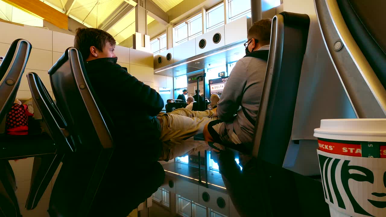 Two young Caucasian men wearing mask having a conversation while waiting to board plane
