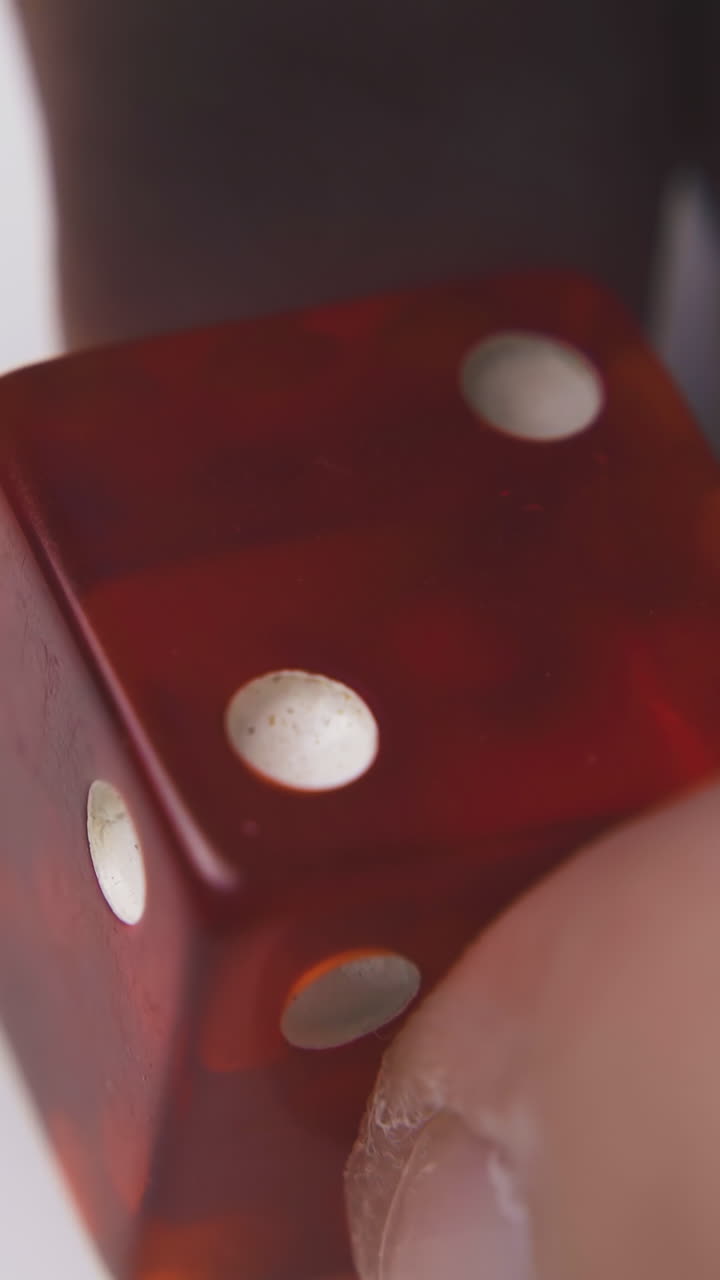 man shows bright red transparent dice with white spots on sides in light background extreme close view