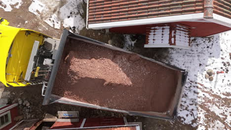el camión volcador descarga una carga de grava junto al edificio rojo en invierno, el avión no tripulado por encima