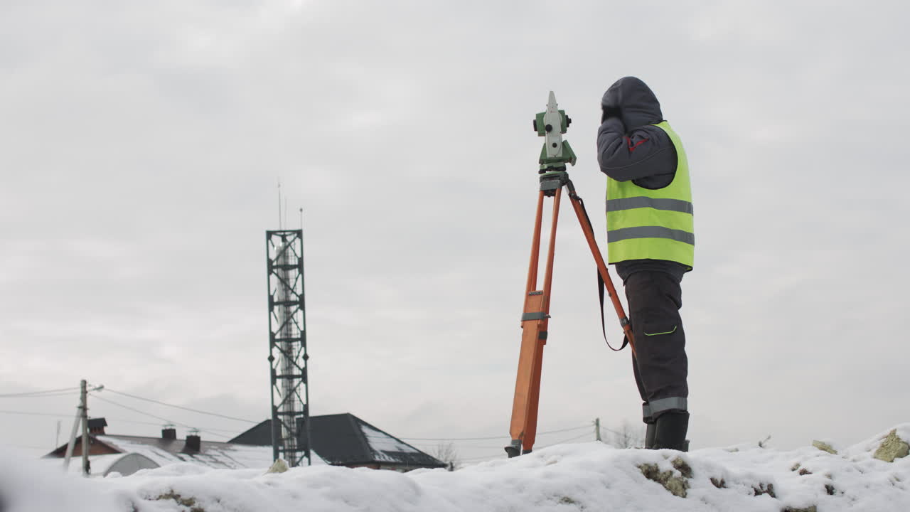 Surveyor using theodolite on a snowy construction site