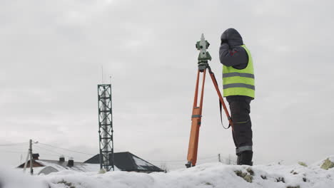 surveyor using theodolite on a snowy construction site