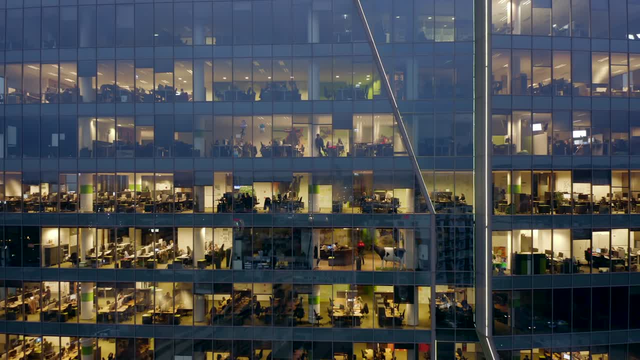 Nahaufnahme der nächtlichen Bürofenster eines Wolkenkratzers mit Menschen, die spät nachts an Computern arbeiten