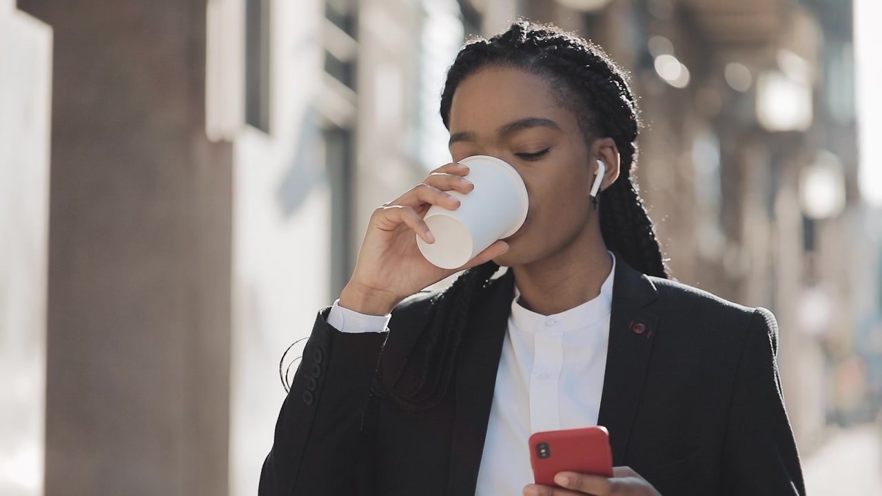Professionel kvinde bruger smartphone og drikker kaffe udendørs
