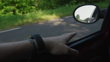 hand of car driver resting next to the rear view mirror, clear road summer day