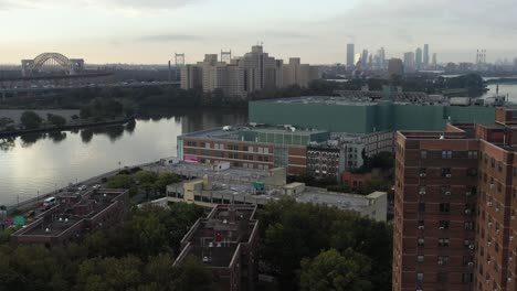 fast-aerial-pan-across-Harlem-River-in-New-York-City,-view-of-housing-project-and-Hellgate-Bridge