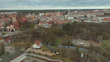 Luftaufnahme-Von-Olsztyn,-Polen,-Ansammlungen-Traditioneller-Und-Moderner-Architektur,-Rote-Ziegeldächer,-Historische-Bauwerke,-Der-Gewundene-Fluss-Łyna,-Im-Hintergrund-Das-Grün-Der-Stadt-Und-Bedeckter-Himmel