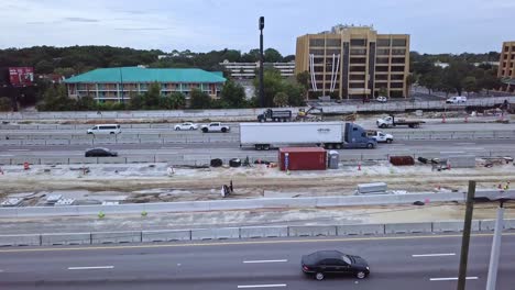 toma aérea baja de un dron de una carretera muy transitada con una zona de construcción de carreteras que muestra automóviles, camiones y edificios en segundo plano.