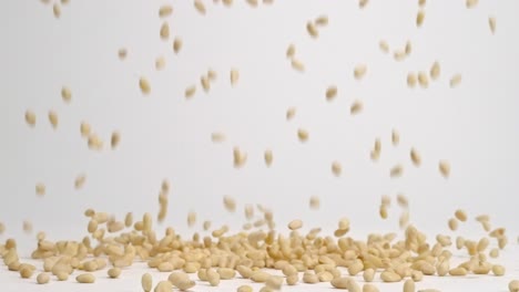 ivory pine nuts raining down on white back drop and bouncing into a pile in slow motion