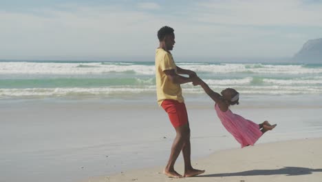 Juguetón-Padre-Afroamericano-Haciendo-Girar-A-Su-Hija-En-La-Playa