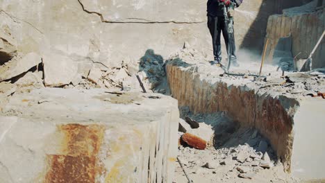 working male builder at a stone quarry crushes stone with a rock-drill. mining of sandstone slabs using hammer