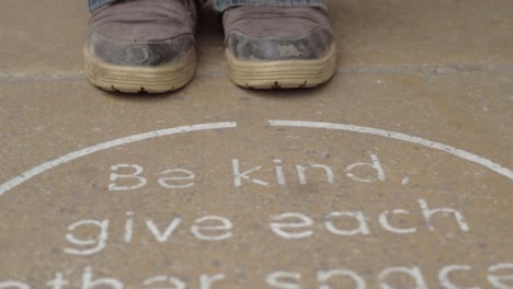 social distancing sign on pavement floor with person waiting