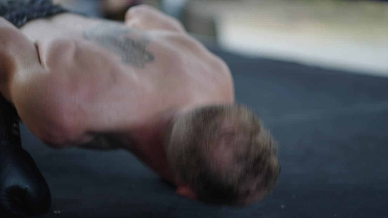 A man performs push-ups in boxing gloves on a mat