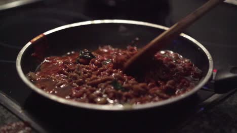 minced meat on a frying pan is mixed with a wooden spoon and then its let to rest