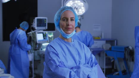 portrait of caucasian female surgeon in lowered face mask smiling to camera in operating theatre