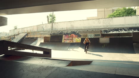 casual bmx rider performing tricks on ramp with bike at city skate park.