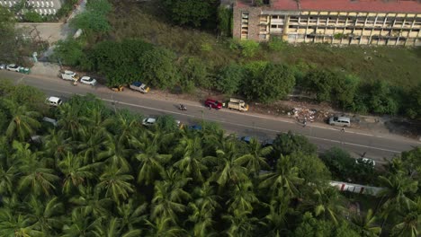 Aerial-shot-of-red-car-in-the-middle-of-the-street-with-coconut-trees-nearby