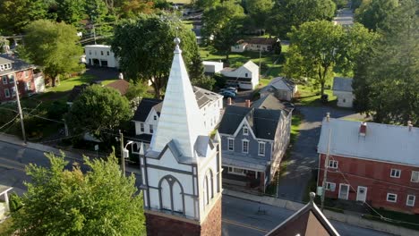 aerial tilt reveals church steeple along road in old historic houses in usa, small town america, august summer magic hour overhead view